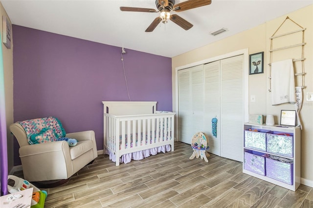 bedroom featuring a closet, ceiling fan, light wood-type flooring, and a crib