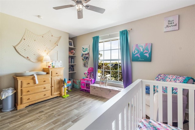 bedroom featuring a crib, ceiling fan, and light hardwood / wood-style flooring