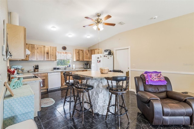 kitchen featuring ceiling fan, white appliances, a breakfast bar, vaulted ceiling, and dark tile flooring