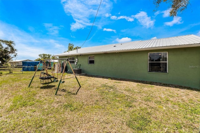 back of house with central AC unit, a playground, and a yard