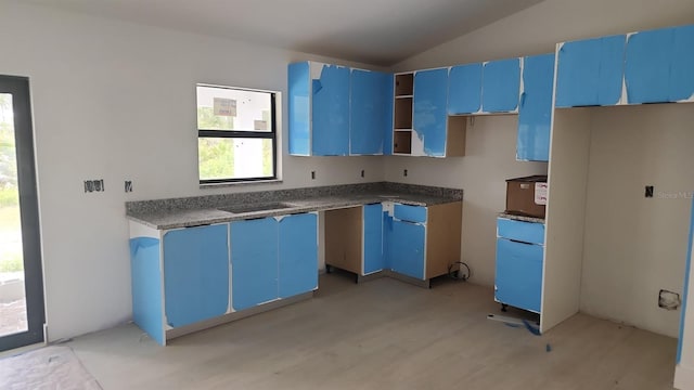 kitchen featuring blue cabinets, dark stone countertops, and lofted ceiling