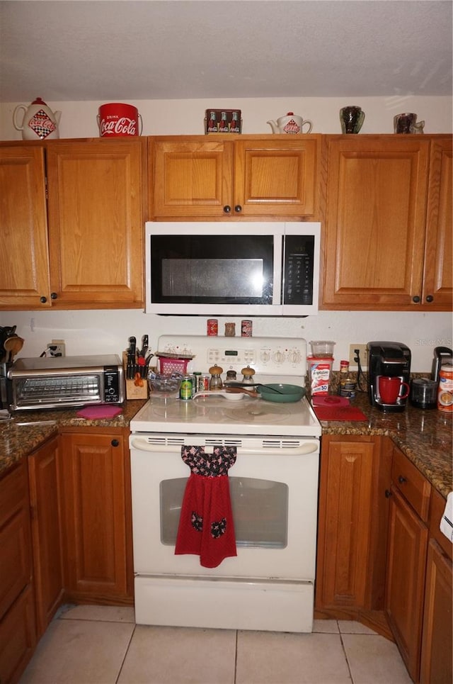 kitchen with white appliances, dark stone counters, and light tile flooring