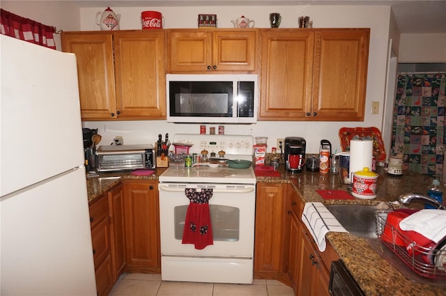 kitchen with white appliances, dark stone countertops, and light tile floors