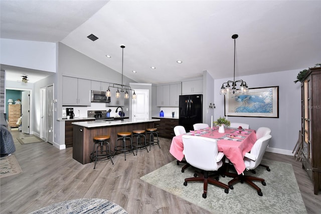 dining area with high vaulted ceiling, an inviting chandelier, light hardwood / wood-style floors, and sink