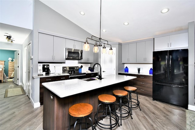 kitchen with light wood-type flooring, vaulted ceiling, decorative light fixtures, and appliances with stainless steel finishes