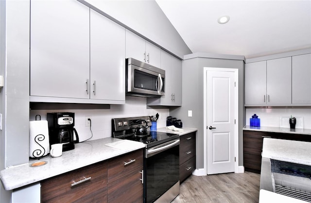 kitchen with light wood-type flooring, stainless steel appliances, vaulted ceiling, dark brown cabinets, and tasteful backsplash