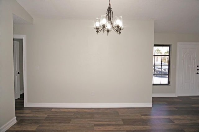 spare room featuring a chandelier and dark wood-type flooring