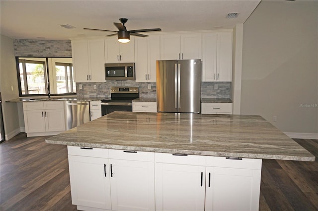 kitchen with backsplash, ceiling fan, stainless steel appliances, white cabinets, and a kitchen island