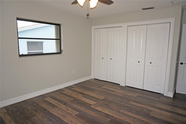 unfurnished bedroom with two closets, ceiling fan, and dark wood-type flooring