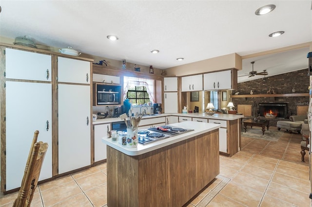 kitchen featuring kitchen peninsula, lofted ceiling, ceiling fan, a fireplace, and light tile floors