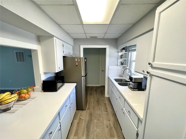 kitchen with white cabinetry, sink, light hardwood / wood-style flooring, a drop ceiling, and stainless steel refrigerator