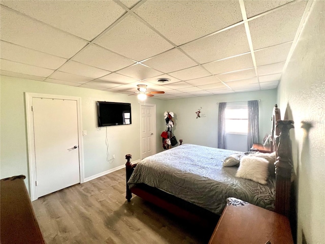 bedroom with wood-type flooring, ceiling fan, and a drop ceiling