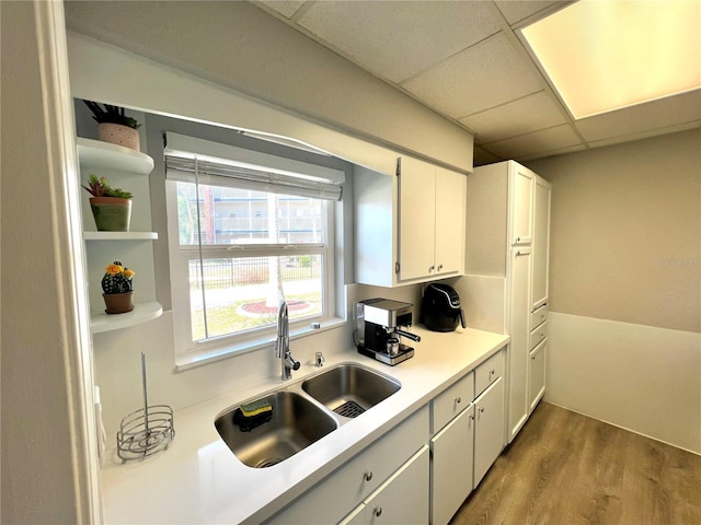 kitchen featuring white cabinets, light hardwood / wood-style floors, a paneled ceiling, and sink