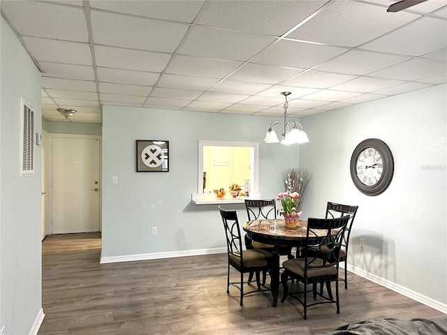 dining space featuring a notable chandelier, a drop ceiling, and dark hardwood / wood-style flooring