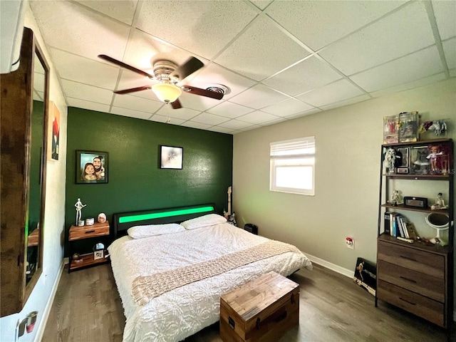 bedroom with dark hardwood / wood-style flooring, ceiling fan, and a drop ceiling