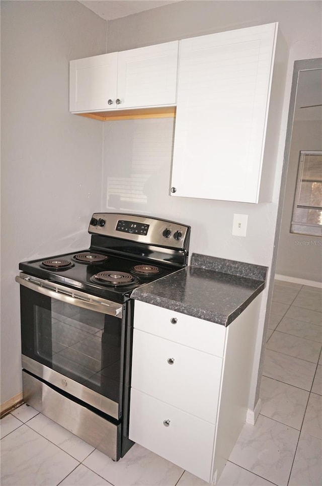 kitchen featuring white cabinets, stainless steel range with electric cooktop, dark stone countertops, and light tile floors