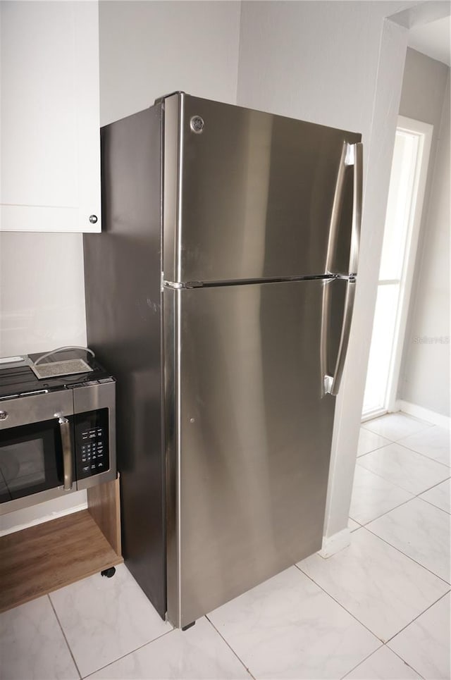 kitchen with stainless steel fridge, light tile floors, and white cabinetry