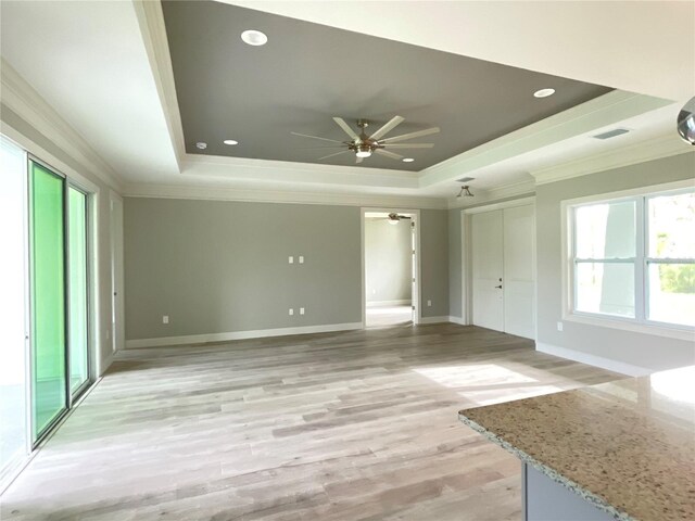 unfurnished living room featuring light hardwood / wood-style floors, ceiling fan, a raised ceiling, and crown molding