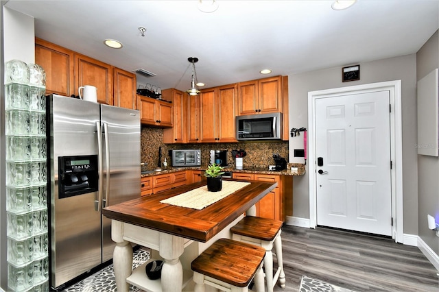 kitchen with a kitchen breakfast bar, appliances with stainless steel finishes, dark stone countertops, dark wood-type flooring, and tasteful backsplash