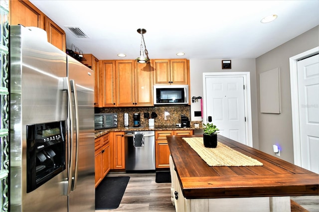 kitchen featuring appliances with stainless steel finishes, light hardwood / wood-style flooring, a center island, tasteful backsplash, and pendant lighting