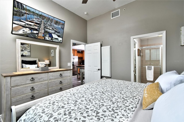 bedroom with ceiling fan, stainless steel fridge with ice dispenser, a high ceiling, ensuite bath, and hardwood / wood-style flooring