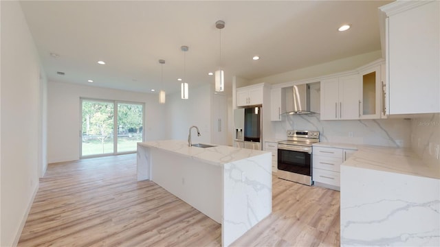 kitchen featuring white cabinetry, wall chimney range hood, decorative light fixtures, a center island with sink, and appliances with stainless steel finishes