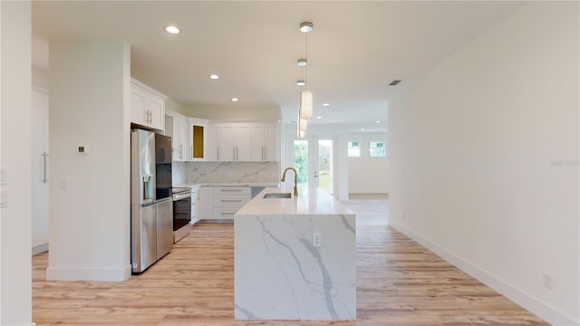 kitchen featuring sink, hanging light fixtures, an island with sink, tasteful backsplash, and white cabinetry