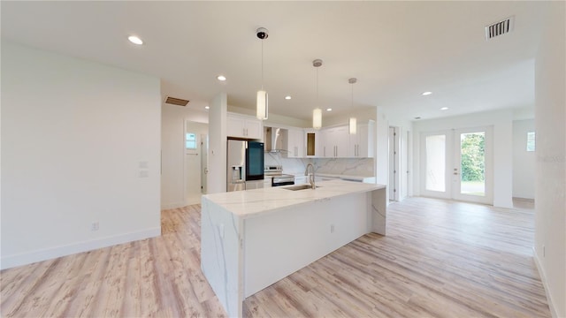 kitchen featuring light stone countertops, appliances with stainless steel finishes, tasteful backsplash, wall chimney exhaust hood, and white cabinets