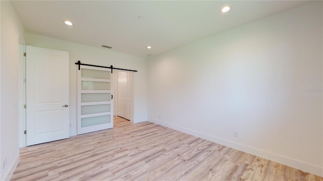 unfurnished bedroom featuring a barn door and light hardwood / wood-style floors