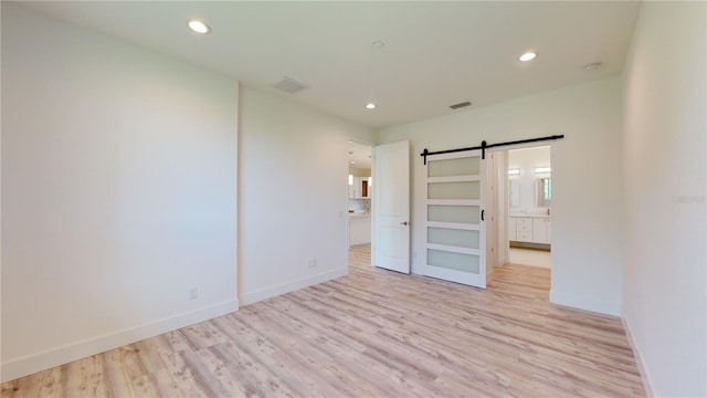 unfurnished bedroom with a barn door, ensuite bath, and light hardwood / wood-style flooring