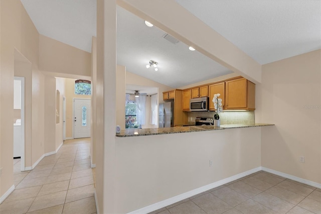 kitchen with stone counters, vaulted ceiling, light tile floors, and appliances with stainless steel finishes