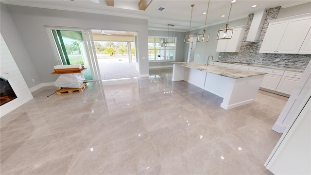 kitchen featuring decorative light fixtures, white cabinetry, a healthy amount of sunlight, a kitchen island with sink, and light stone counters