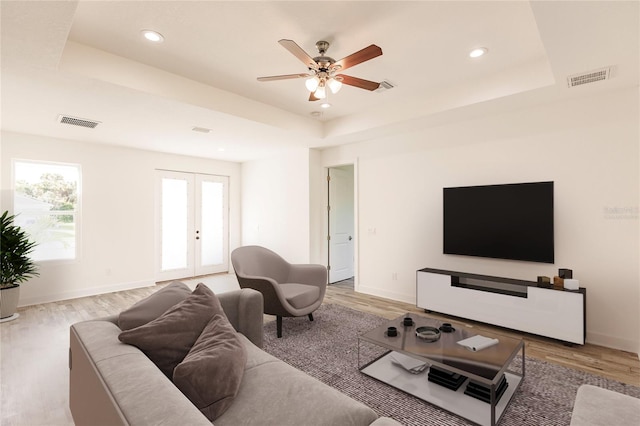 living room featuring a raised ceiling, ceiling fan, french doors, and light wood-type flooring