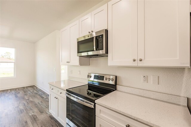 kitchen with light stone counters, stainless steel appliances, white cabinetry, and light wood-type flooring