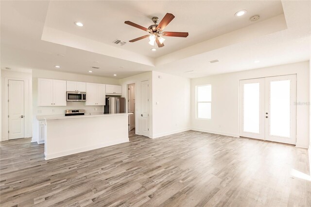 kitchen with stainless steel appliances, a center island, french doors, white cabinetry, and a raised ceiling