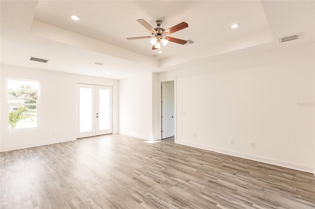 unfurnished room featuring a tray ceiling, light hardwood / wood-style floors, ceiling fan, and french doors