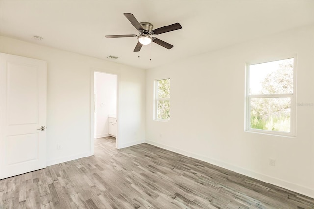 unfurnished bedroom with ensuite bath, light wood-type flooring, ceiling fan, and multiple windows