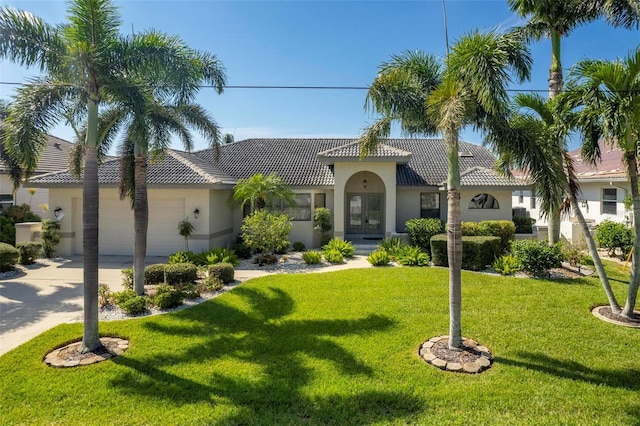 mediterranean / spanish house with a tile roof, stucco siding, a garage, driveway, and a front lawn