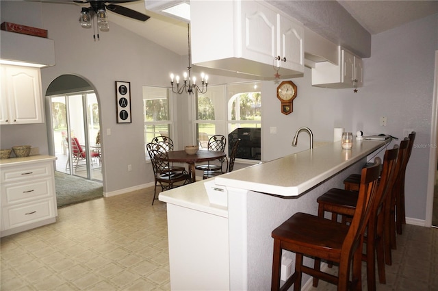 kitchen with a healthy amount of sunlight, a kitchen breakfast bar, white cabinetry, and ceiling fan with notable chandelier