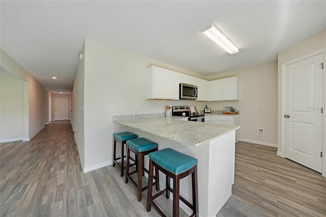 kitchen featuring stainless steel appliances, light stone countertops, a breakfast bar area, white cabinetry, and light wood-type flooring