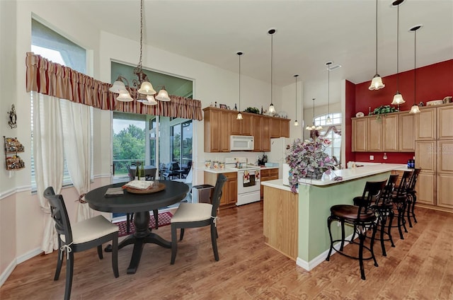 kitchen featuring light hardwood / wood-style floors, a notable chandelier, a kitchen bar, white appliances, and hanging light fixtures