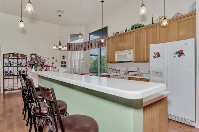 kitchen featuring a breakfast bar area, white appliances, decorative light fixtures, and light hardwood / wood-style flooring