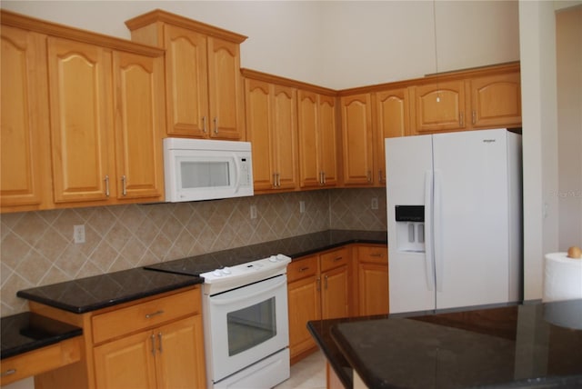 kitchen with tasteful backsplash, dark stone counters, and white appliances