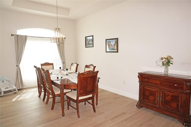 dining space featuring a tray ceiling, light hardwood / wood-style floors, and an inviting chandelier