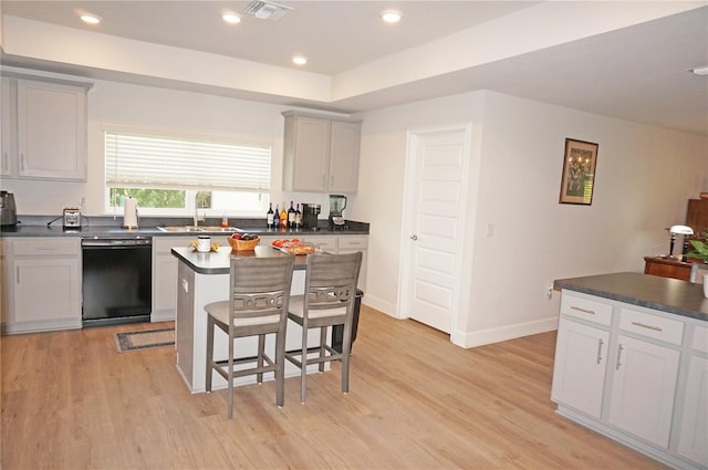 kitchen with light hardwood / wood-style floors, a center island, black dishwasher, a breakfast bar area, and sink