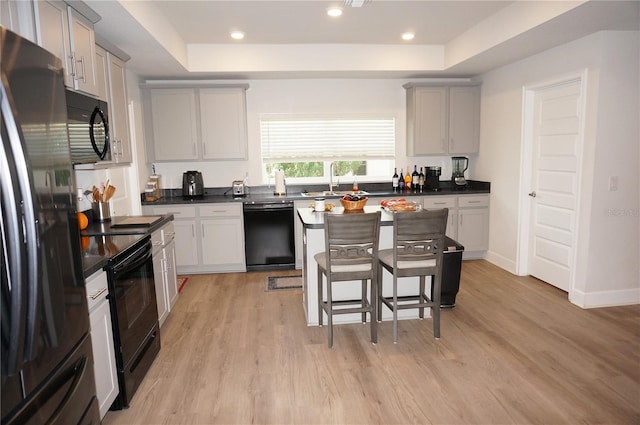 kitchen with a raised ceiling, light hardwood / wood-style floors, and black appliances