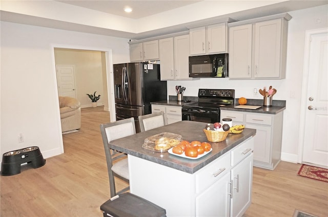 kitchen featuring light hardwood / wood-style floors, a kitchen island, a breakfast bar, black appliances, and white cabinets