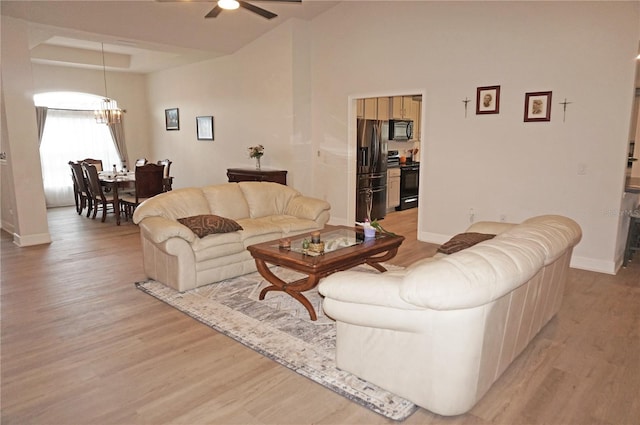 living room featuring a raised ceiling, light hardwood / wood-style floors, ceiling fan with notable chandelier, and a high ceiling