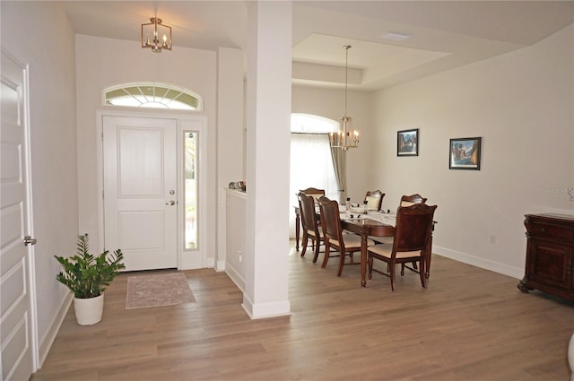 foyer entrance featuring a raised ceiling, light hardwood / wood-style floors, and a notable chandelier