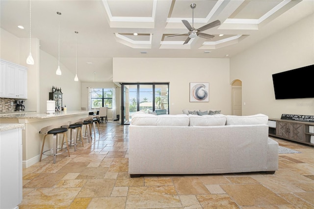 living room with light tile floors, coffered ceiling, ceiling fan, and beamed ceiling